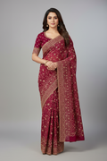Woman wearing a maroon saree with gold patterns on a gray background